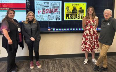 Aurora Bacowsky and Gracie Duncan, recent NIC graduates, stand center in front of their winning poster designs from the PIA Student Poster Contest. NIC Professors Lydia Ramus and Philippe Valle stand at left and right, respectively.